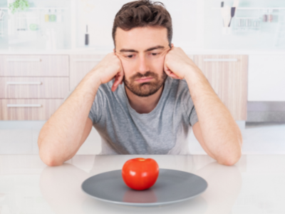 A young man eating less to lose weight staring at an apple  on a plate