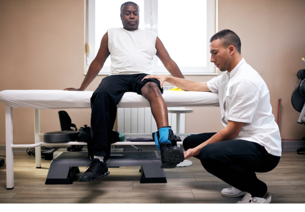 Physical Therapist works with African American middle age male performing a knee extension exercise with weight on